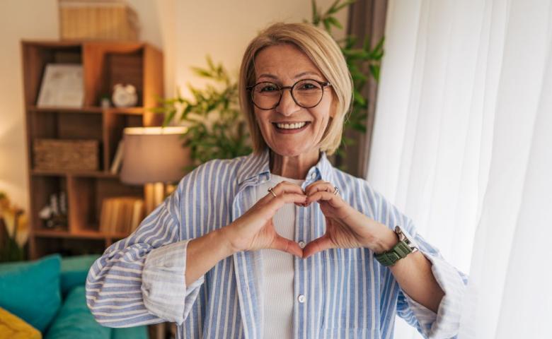Woman holding up hands in heart shape in living room