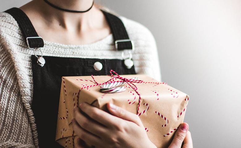 Obscured face of a woman in overalls holding a Christmas gift