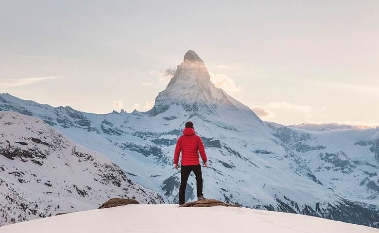 Person standing on top of snowy mountain looking ahead to another mountain peak