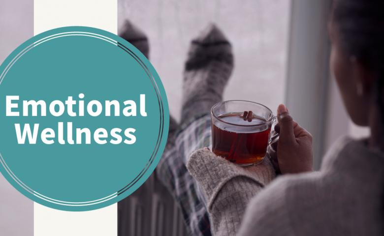 A person sitting with a cup of tea with the words &quot;Emotional Wellness&quot; in a teal coloured, circular graphic on the left side of the photo.