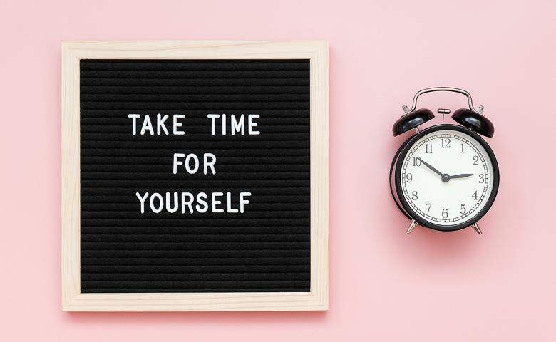 Pink background with a felt letter board stating &quot;take time for yourself&quot; alongside a clock