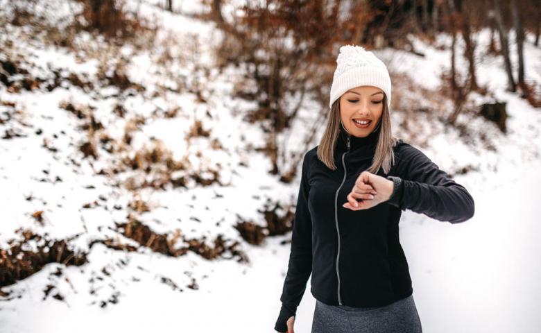 Woman walking on a snowy path looking at her smartwatch