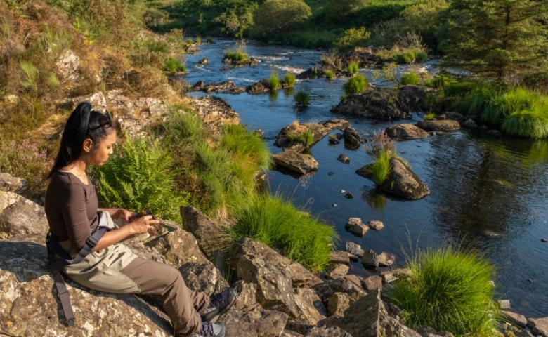 Woman sitting by a rocky river bed getting ready to go fly fishing