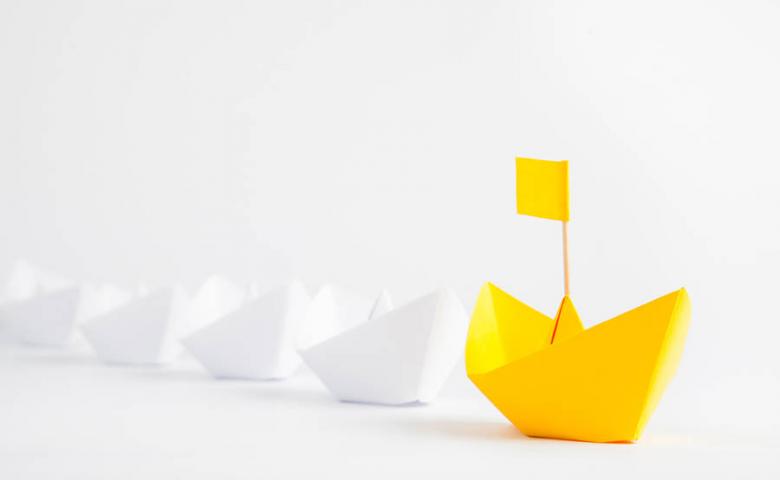 Yellow paper ship leading multiple white paper ships